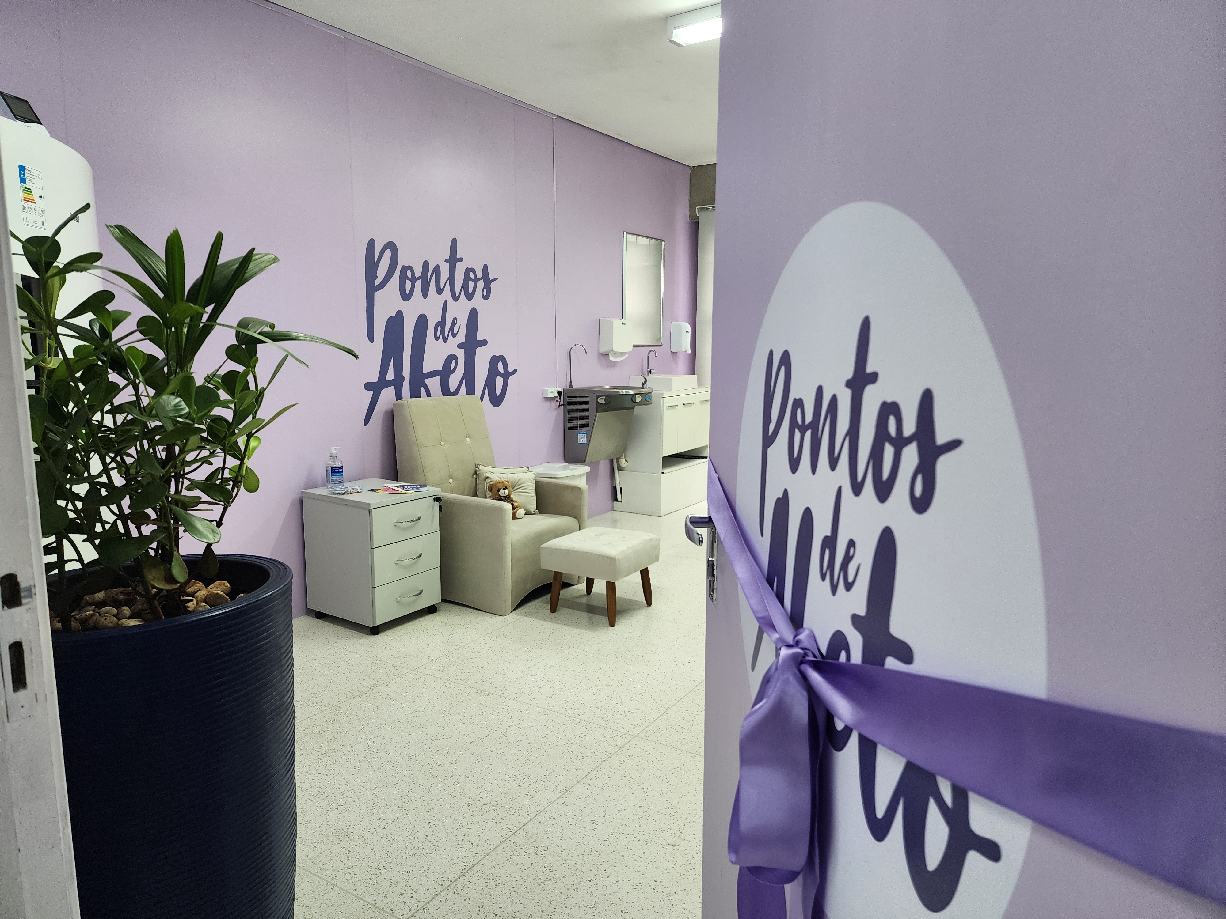 Imagem da décima sala Pontos de afeto. No centro vemos uma poltrona Branca com um urso de pelucia em frente a uma parede lilás com o logotipo do programa na cor roxa escuro. Do lado direito da imagem vemos a porta da sala na cor lilás com o logotipo do programa.
